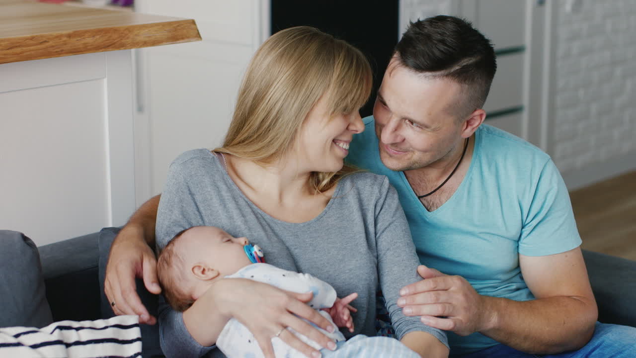 집에서 웃고 있는 그녀의 팔에 아기를 안고 있는 젊은 행복한 가족