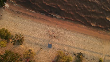 una toma aérea dinámica de arriba hacia abajo de un grupo de amigos jugando voleibol en la playa durante la puesta de sol