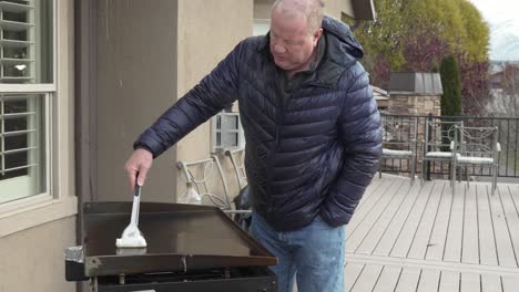 mature man wiping down his flat top griddle with oil after a cook