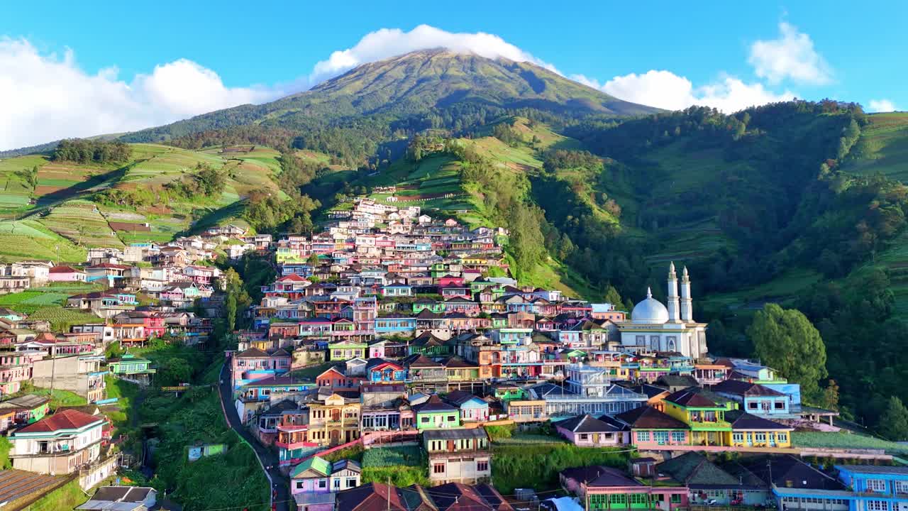 Aerial view of Nepal van Java village nestled on the lush slopes of Mount Sumbing, Indonesia. The colorful houses and terraced hills create a stunning mountain landscape under a bright blue sky
