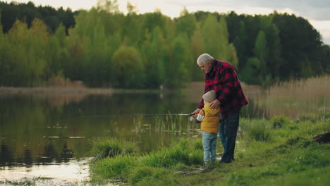 el niño está aprendiendo a pescar en la orilla del lago. el abuelo amoroso está ayudando.