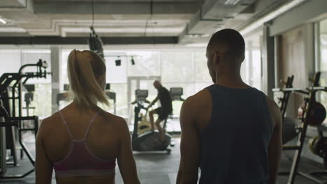 vista trasera de una mujer caucásica y un atlético afroamericano en el gimnasio.