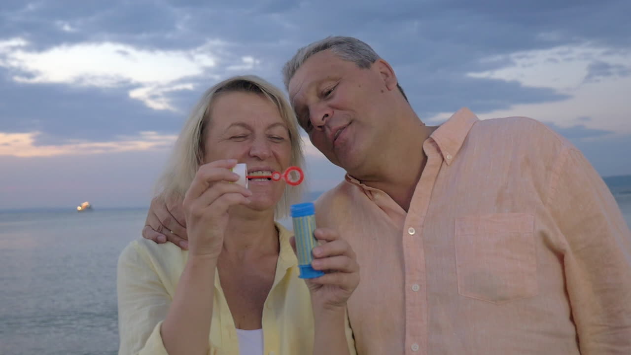 una pareja de mayores soplando burbujas en la orilla del mar