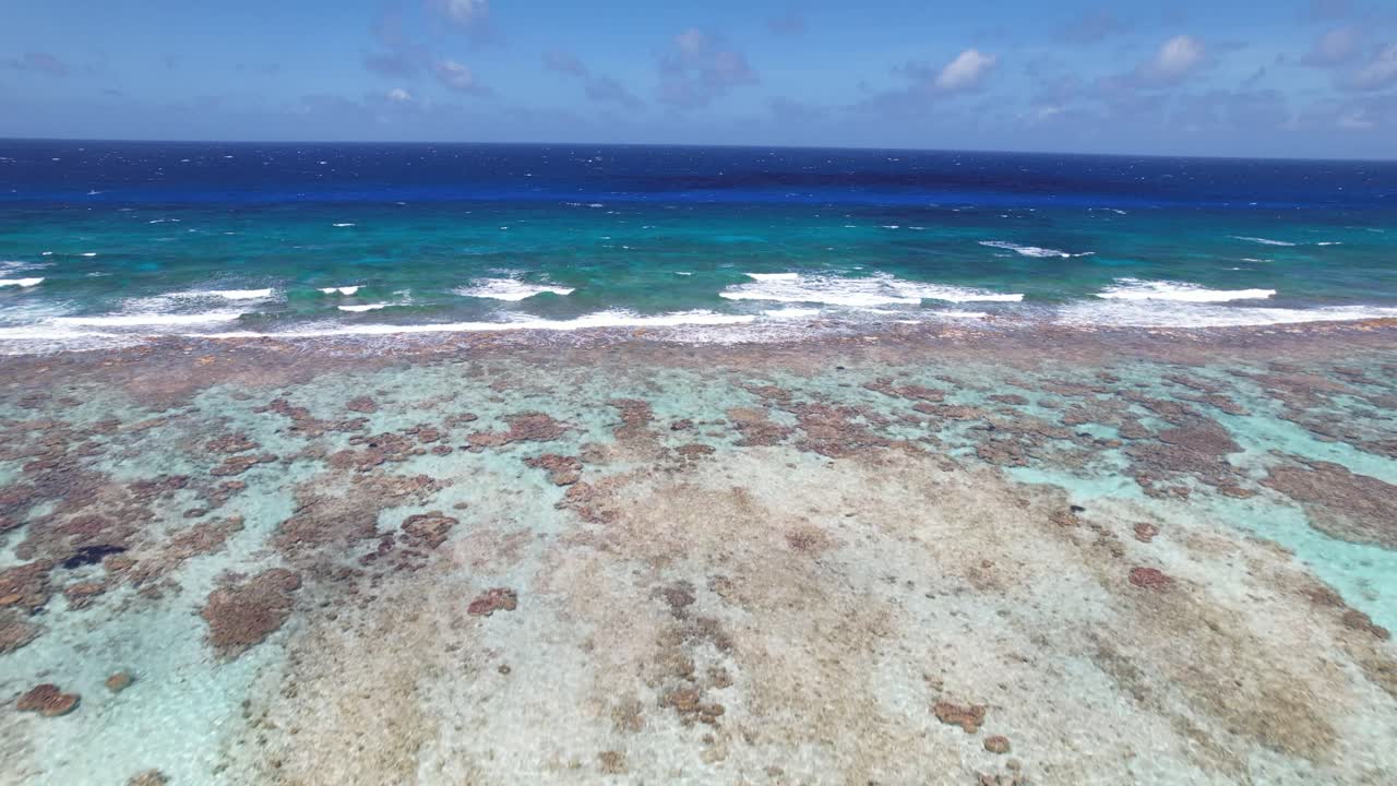 aguas claras de color turquesa y ondas suaves sobre un arrecife de coral en los rocas, movimiento aéreo hacia adelante