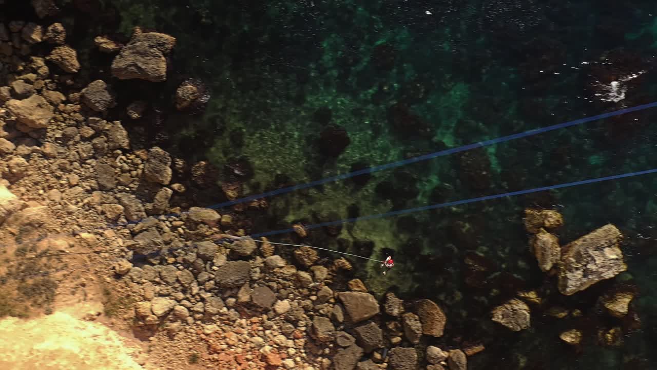 tiro de acción de bungee saltando desde un acantilado en una tirolesa sobre el mar