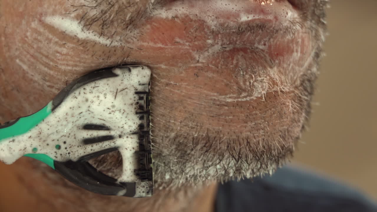 Close up of a man shaving his beard with a green and black razor