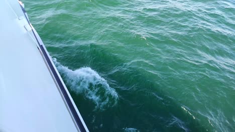 On-board-the-boat-sailing-in-Rías-Baixas-seen-from-the-top-of-the-side-and-the-greenish-sea-water-that-gives-off-foam,-sunny-day,-shot-blocked-down,-Pontevedra,-Galicia,-Spain