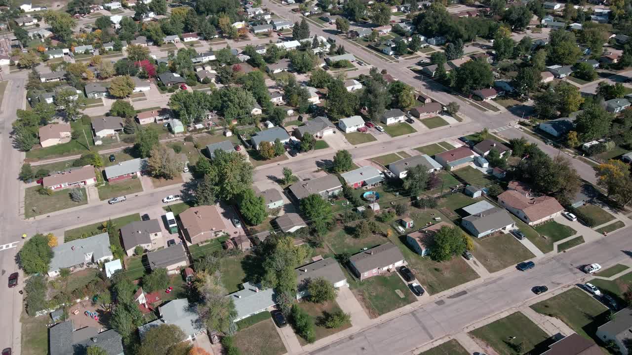 A drone flying towards houses before panning up and revealing more of a neighborhood in the background