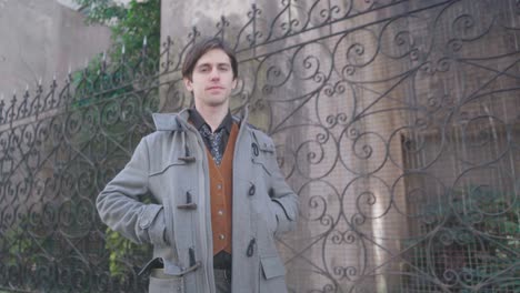 young man in shirt, tie and waistcoat, walks towards camera with hands in coat pockets
