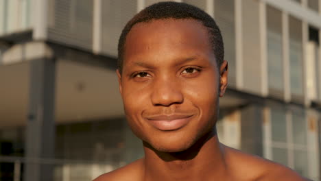 portrait of young black man smiling and looking at camera outdoors. shirtless handsome african american male athlete resting on a sunny afternoon. close-up.