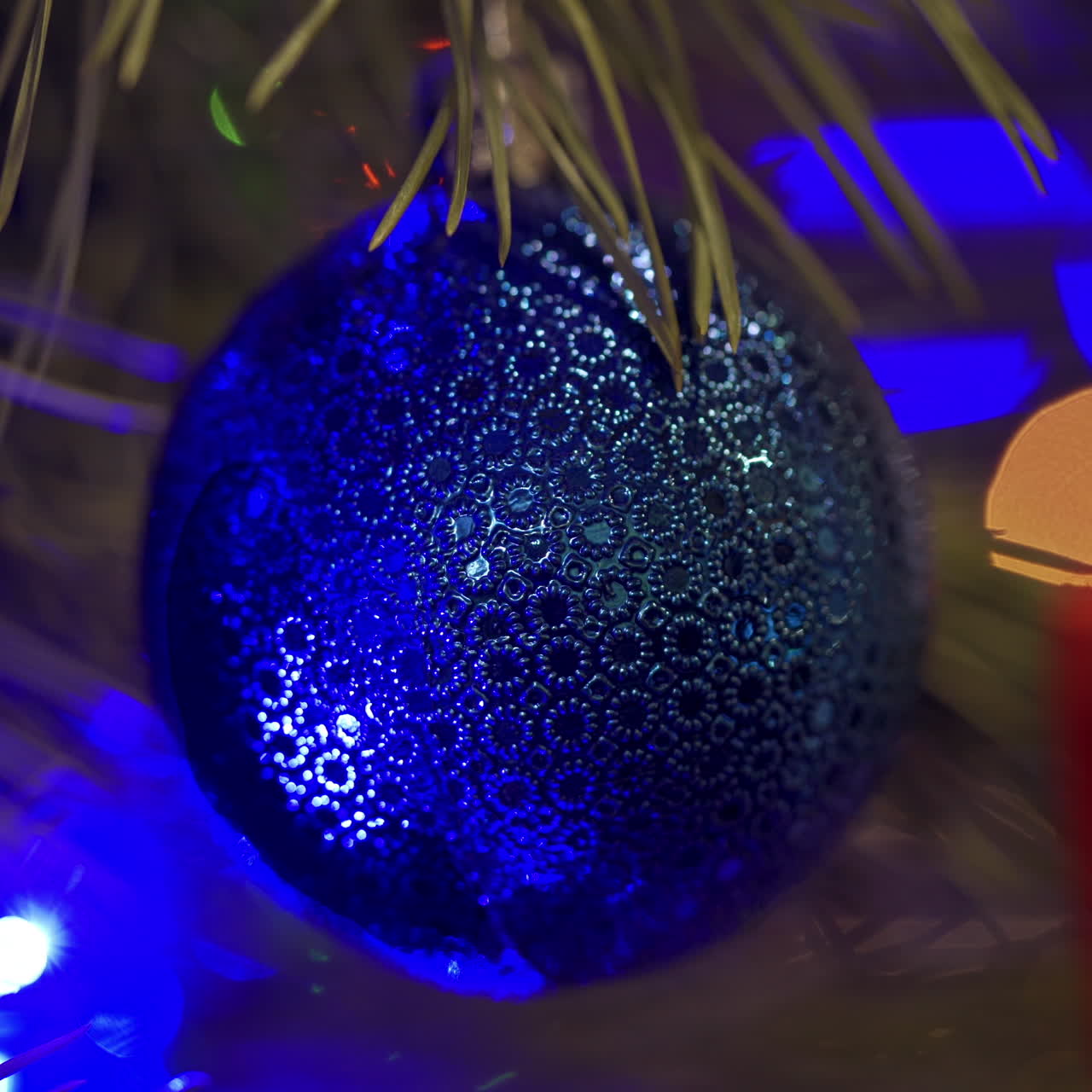 Blue Christmas ball on New Year tree. Lights of blue garland blinking on a holiday toy hanging on a spruce tree. Christmas tree lights twinkling. Close-up.