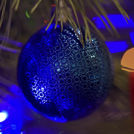 blue christmas ball on new year tree. lights of blue garland blinking on a holiday toy hanging on a spruce tree. christmas tree lights twinkling. close-up.