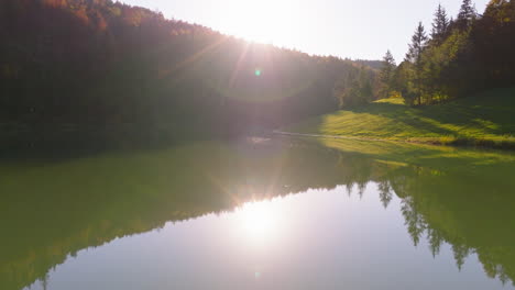 Bavaria-woodland-mountain-sunrays-reflections-shining-in-Sylvenstein-forest-lake-aerial-view-push-in-low-angle