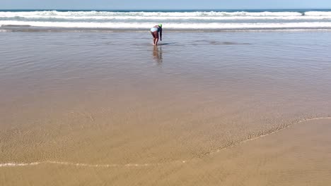 Una-Mujer-Se-Dedica-A-Pescar-Almejas-Mientras-Las-Olas-Traen-Estos-Tesoros-Del-Mar,-Mostrando-La-Armonía-Entre-La-Actividad-Humana-Y-El-Ritmo-Natural-Del-Océano.