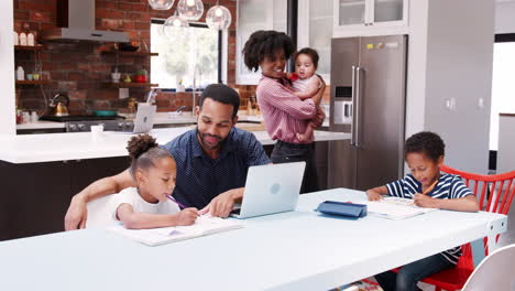 Father-Helps-Children-With-Homework-Whilst-Mother-Holds-Baby