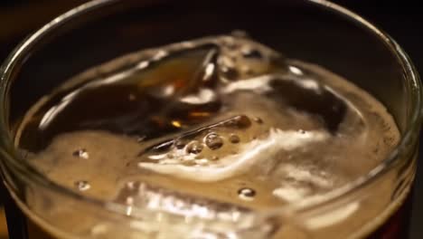 a close-up exploration of refreshing cold beverage with ice cubes melting in a glass, showcasing the foamy texture and bubbles on a relaxed evening