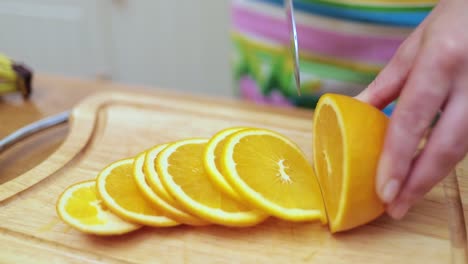 women's hands housewives cut with a knife fresh orange on the cutting board of the kitchen table