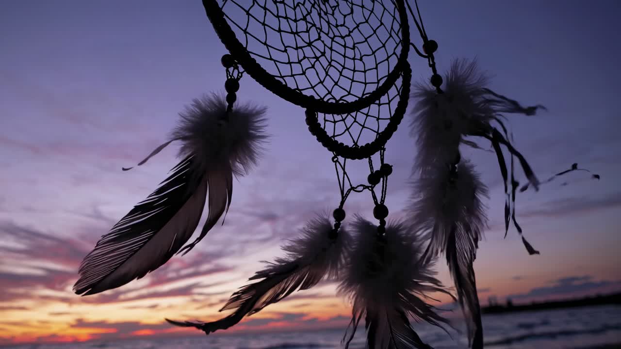 Dreamcatcher with feathers at sunset on a beach. Silhouette of dreamcatcher against colorful sky