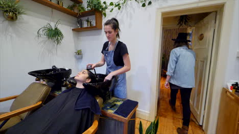 slow mo walking through hair salon with a hairdresser washing a clients hair in a basin