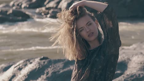 nice lady fixes hair on rocky bank of river at strong wind