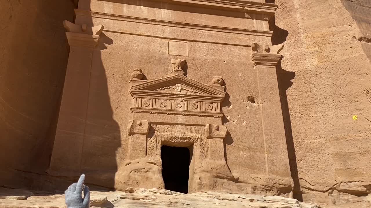 female guide in traditional clothes explaining stories of the decorations of an old tomb at famous tourist destination-Madain Saleh, Saudi Arabia