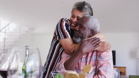 una pareja mayor afroamericana sentada junto a una mesa bebiendo vino cenando y abrazándose