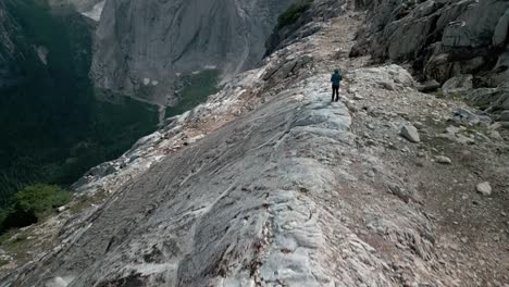 Drone-shoot-starting-on-the-ground,-with-a-hiker-standing-on-the-edge-of-a-remote-valley-with-a-big-granite-wall-on-the-background