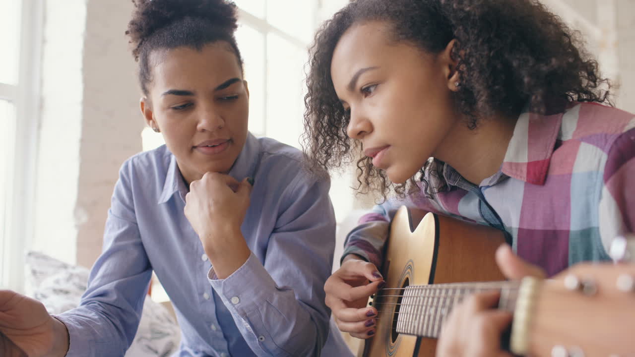 Teenage girl learning guitar from a woman