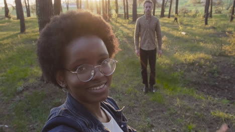 a young girls takes a selfie of her and a friend in the forest and say hello