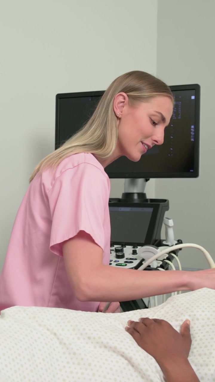 Video verticale: Tecnico in camice rosa che prende il gel e scansiona l'addome con una sonda per un esame in clinica