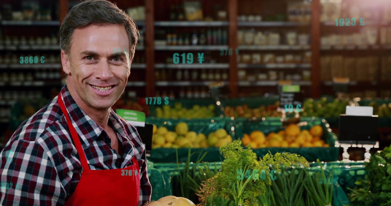 Empleado de frutería ajustando zanahorias y cebollas en una cesta, revelando calabaza y brócoli, sonriendo a la cámara