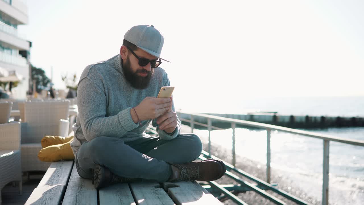 hombre usando un teléfono inteligente en un café de la playa