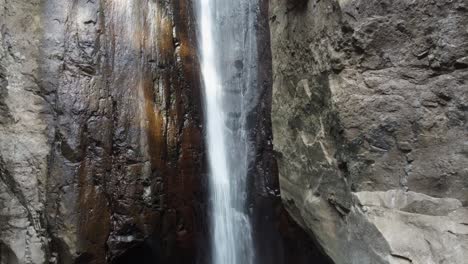 Thin-vertical-waterfall-drops-into-narrow-rock-cliff-stone-grotto