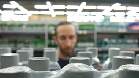 close-up of many plastic bottles of water with white caps on a store shelf and a man takes one