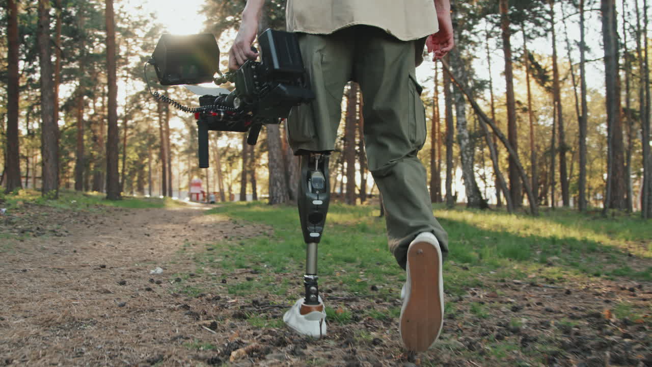 Man With Prosthetic Leg And Video Camera Walking In Forest