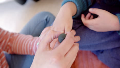 Biracial-mother-sitting-and-painting-daughter's-nails-in-sunny-room