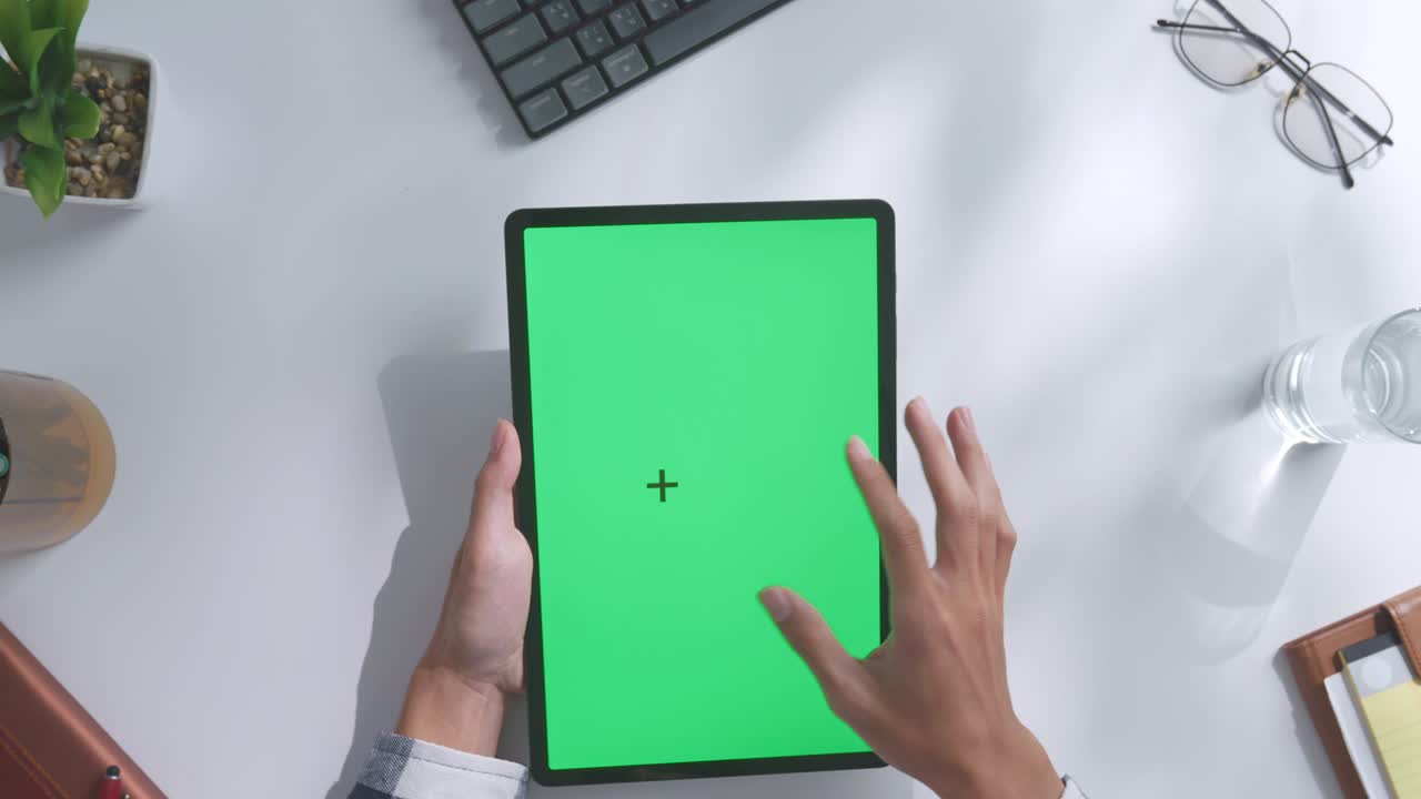 верхний вид ноутбука с макетным зеленым экраном chromakey на деревянном офисном столе рядом с ноутбуком с ручками, очками и стаканом воды.