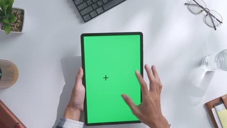 vista de arriba hacia abajo de una computadora portátil con pantalla verde simulada pantalla chromakey en un escritorio de oficina de madera al lado de la libreta con bolígrafos, gafas y un vaso de agua.