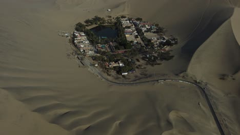 a small lagoon oasis in the middle of the desert surrounded by dunes. drone orbits around to the right while slowly tilting camera up. located in "huacachina" in ica, peru.