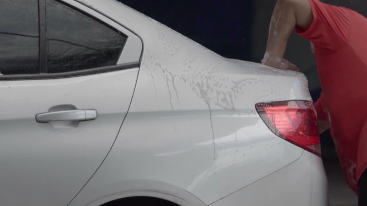 Man washing rear side of a silver car with yellow cloth at a car wash station