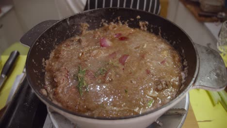 adding water into a deep cooking pot with beef shank, onion slices, celery and spices cooked inside