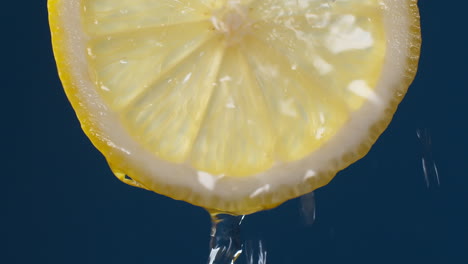 slow motion macro shot of flowing water from lemon slice on blue-black background