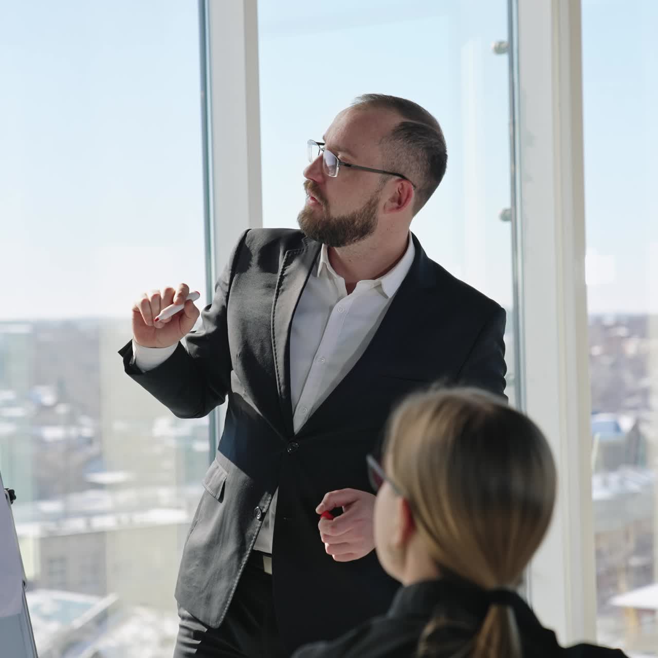 Positive and warm atmosphere at morning meeting. Smiling man makes speech about chart in front of his teammates. Sunlit cityscape at backdrop