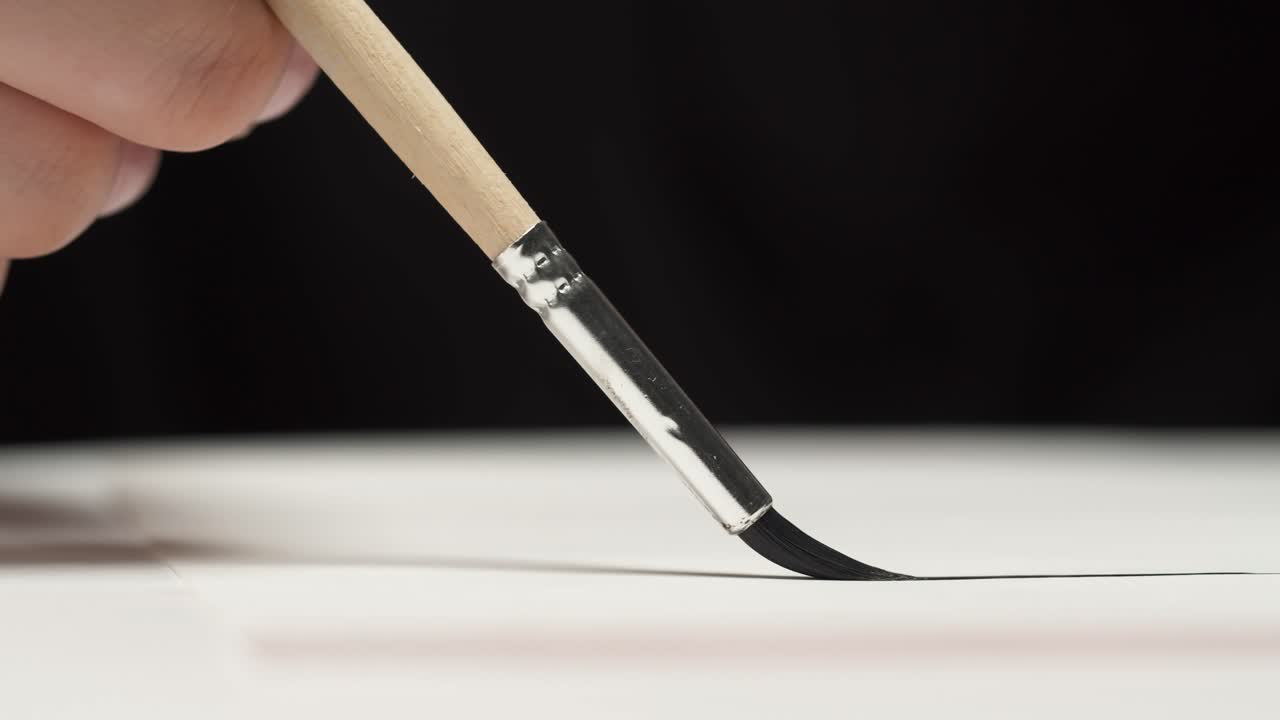 Close-Up of Paintbrush Drawing a Smooth Black Line on White Paper