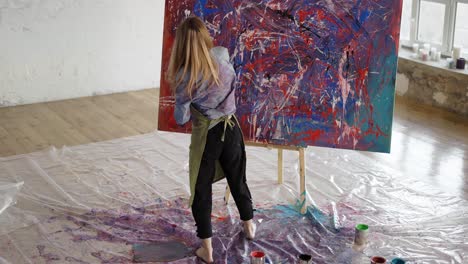 woman paints on canvas emotionally dipping hands in paints jar, rare view