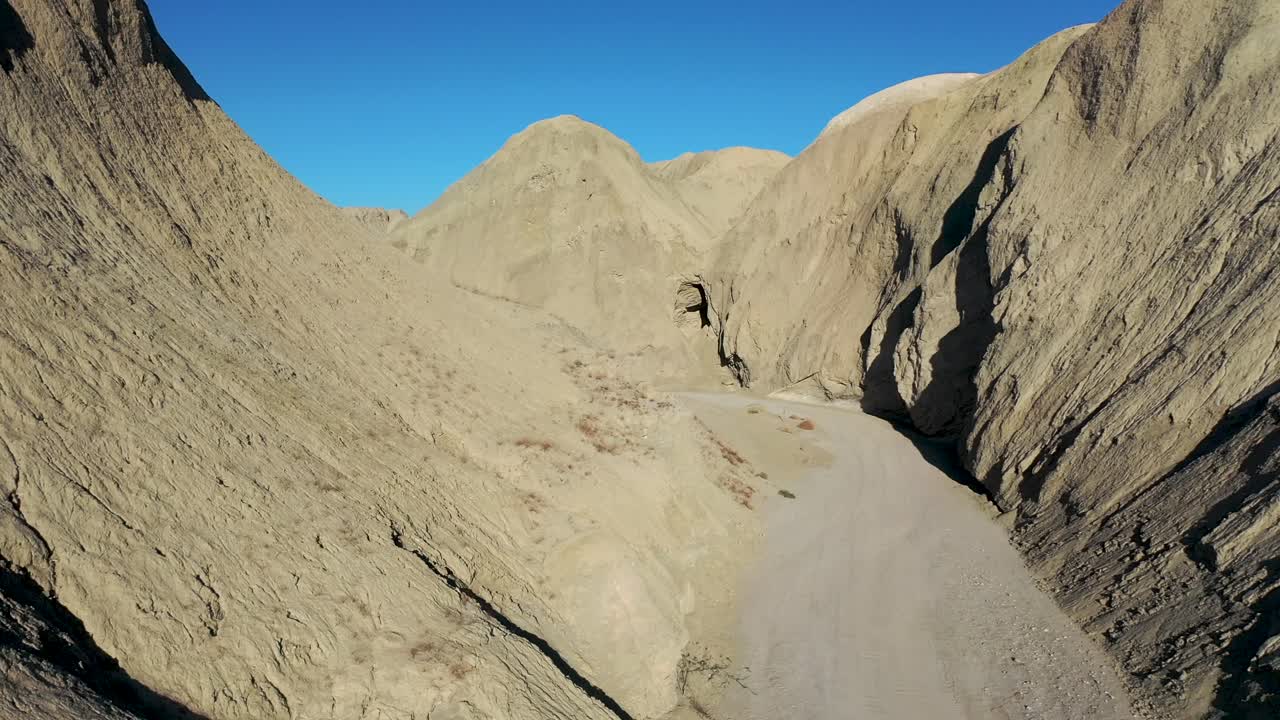 vuelo aéreo entre laderas formadas por cuevas de barro sobre camino de tierra en un día caluroso y seco - cuevas de barro arroyo tapiado en el parque estatal anza borrego