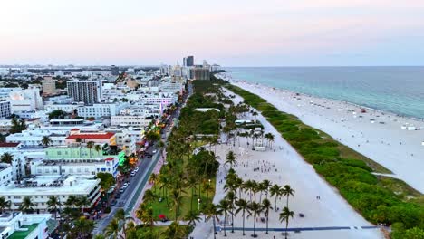 aerial drone zoom out view of south beach in miami, ocean drive street at sunset, buildings, palm trees.