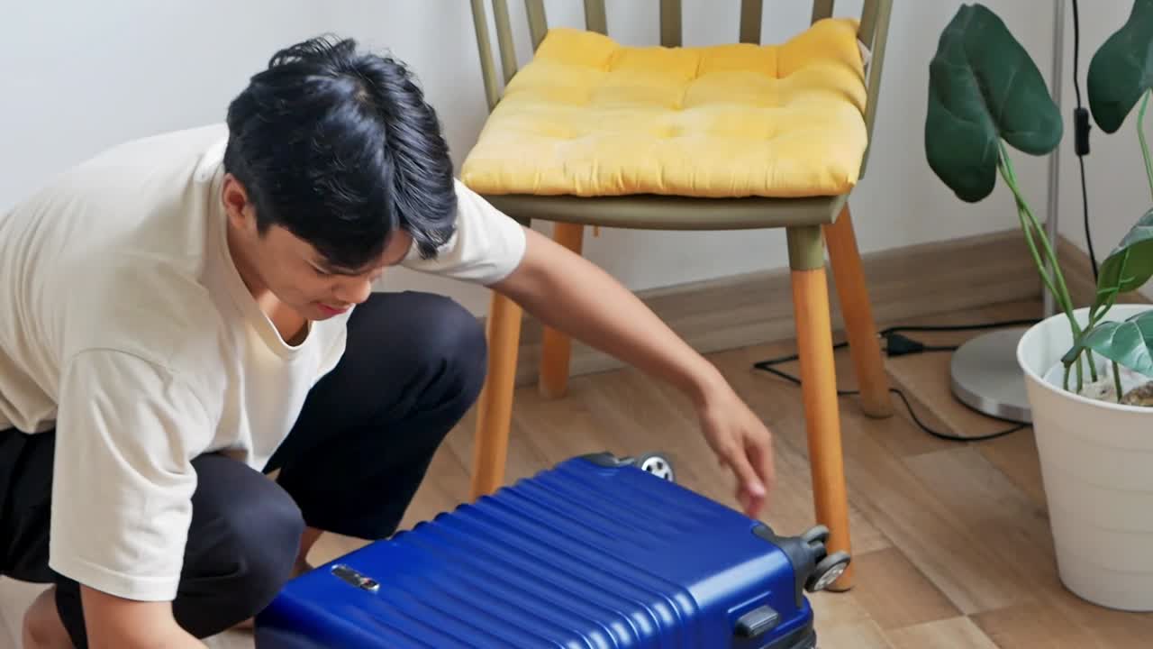 Serious young Asian man putting clothes into blue suitcase prepare for adventure