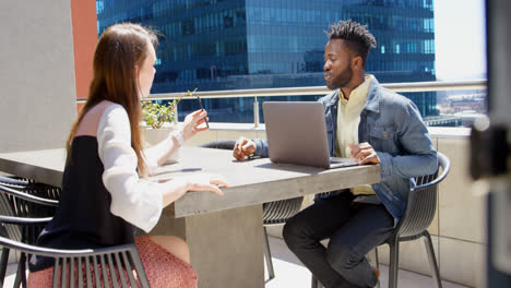 Side-view-of-young-mixed-race-business-team-planning-and-sitting-at-table-in-office-balcony-4k