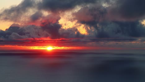 Die-Rote-Sonne-Geht-über-Dem-Ozean-Unter-Und-Färbt-Die-Sich-Bewegenden-Wolken,-Echtzeitaufnahme